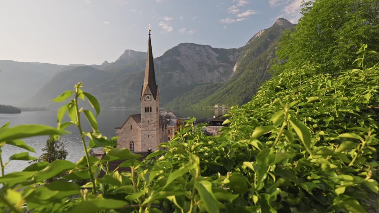 奥地利阿尔卑斯山哈尔施塔特湖上的哈尔施塔特村的万向节镜头。日出时，镜头在奥地利哈尔施塔特村的绿叶间移动。清晨4K拍摄视频素材