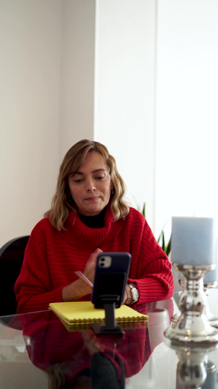 一位拉丁裔妇女，职业是心理学家，正在她的办公室里照顾一个病人，通过她的手机进行视频通话视频下载