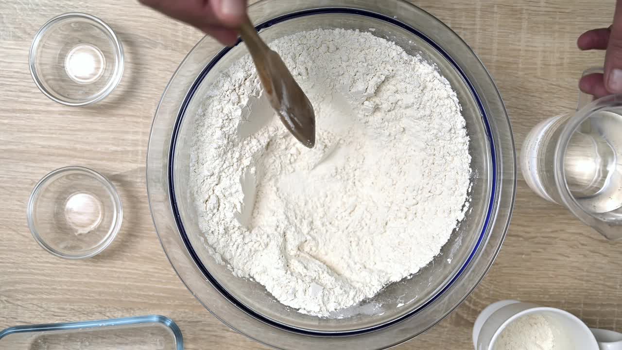 一名男子用手将盐和面粉混合在一起，准备制作美味的自制面包。视频下载