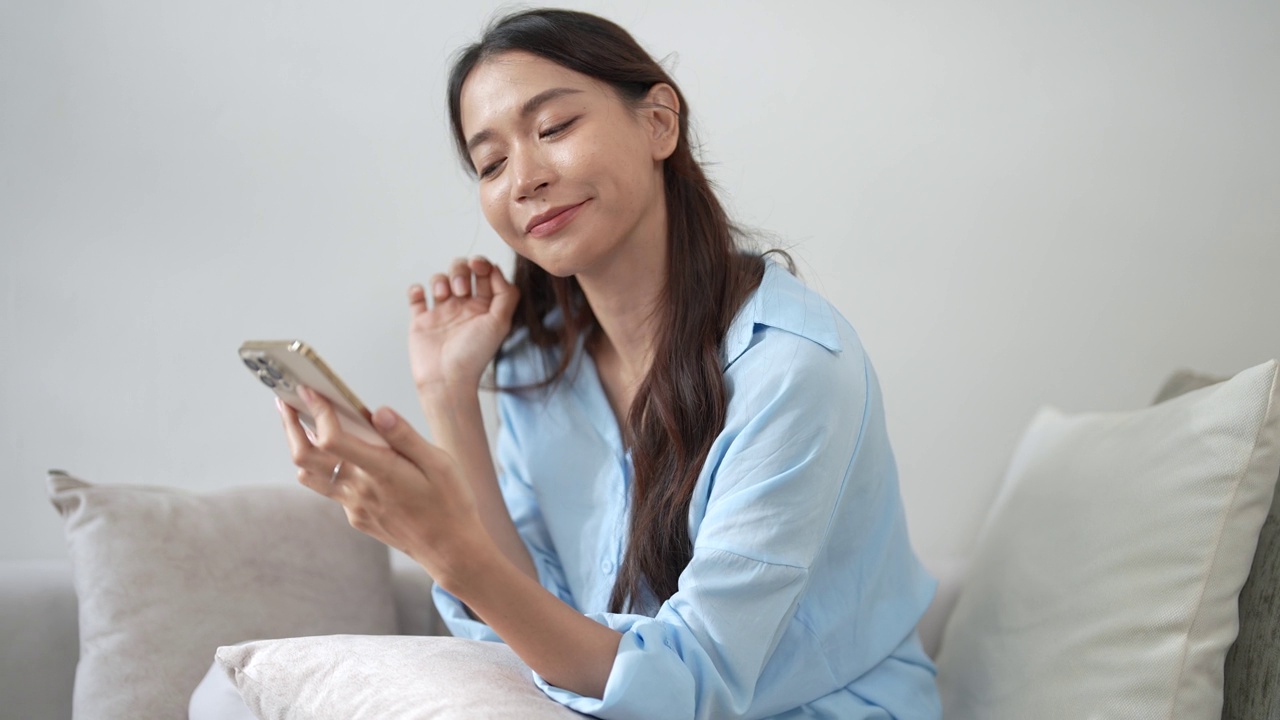 亚洲女性在家客厅使用智能手机。视频下载