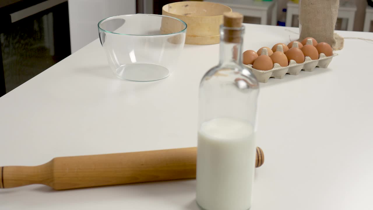 白色的厨房桌子上放着牛奶、鸡蛋和面粉，用来揉面团、烤面包和烘焙产品视频素材
