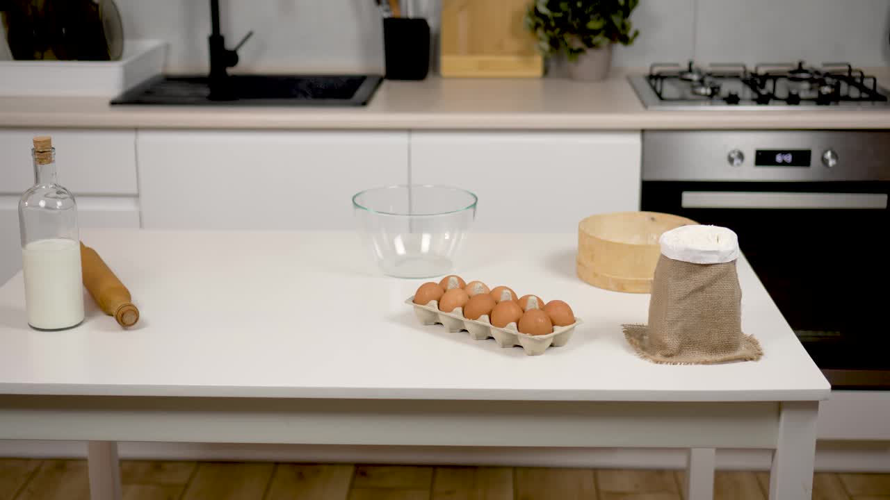 家庭烹饪的概念。白色的木桌上放着装在玻璃瓶里的牛奶、鸡蛋和面粉，桌上摆着为自制面包、煎饼和饼干准备的擀面杖视频素材