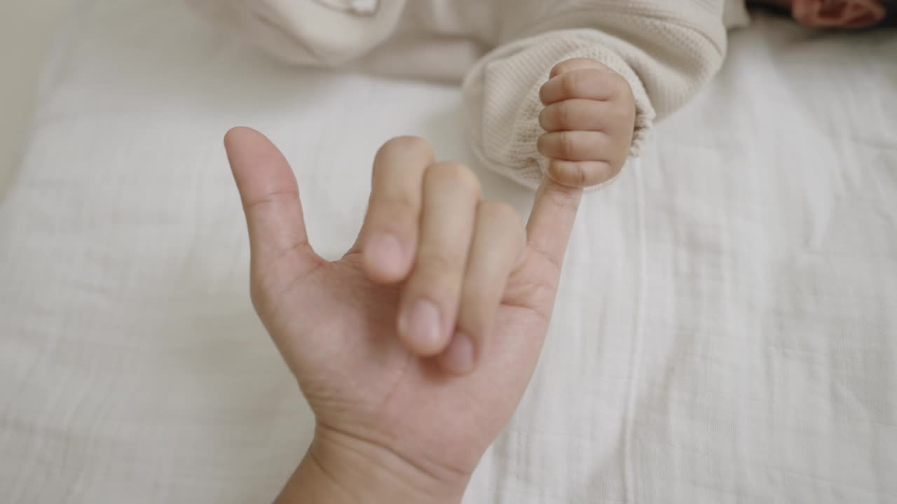 一个小女孩躺在床上看着她的妈妈，握着她的小手指。视频下载