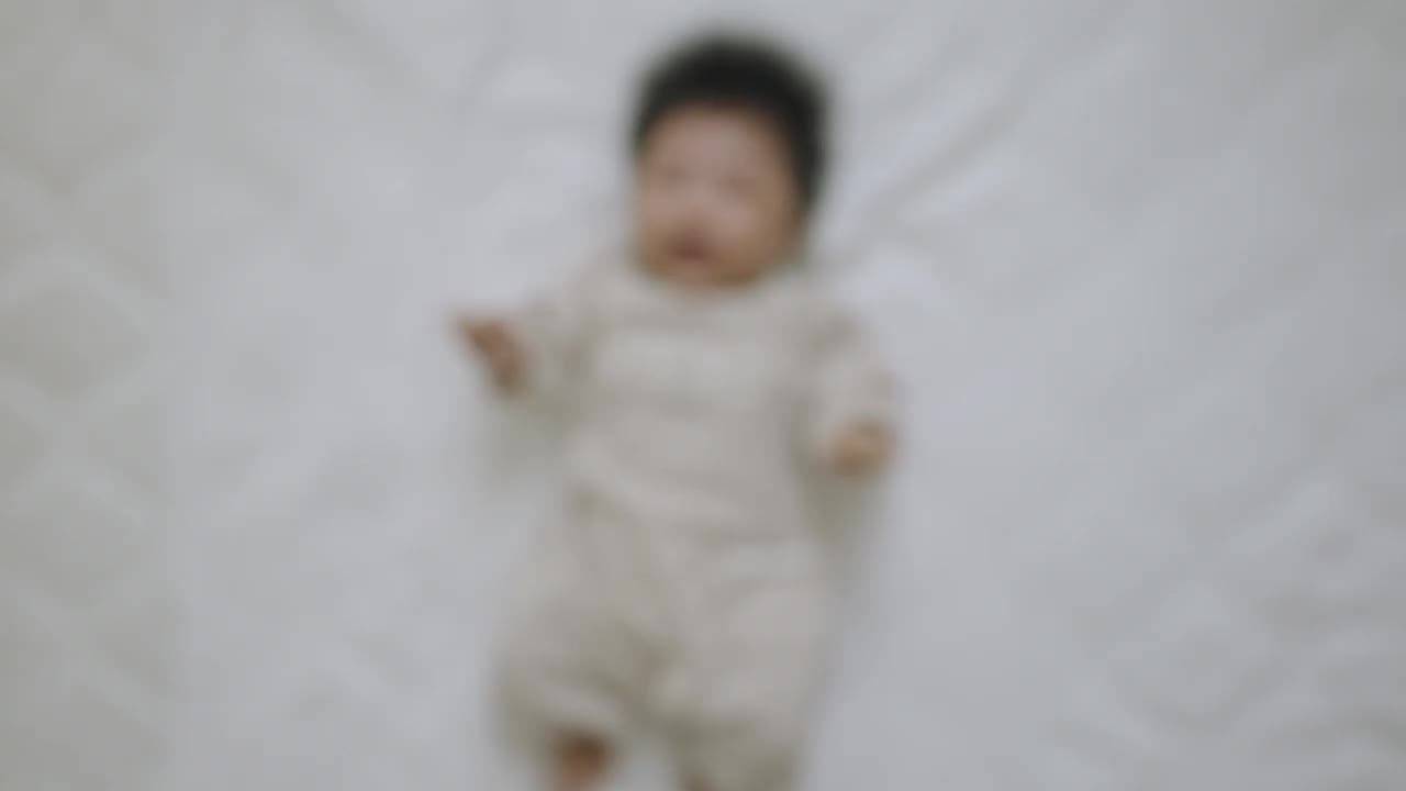 俯视图，一个刚出生的女婴穿着长袖婴儿服，仰面躺在床上蠕动。视频下载