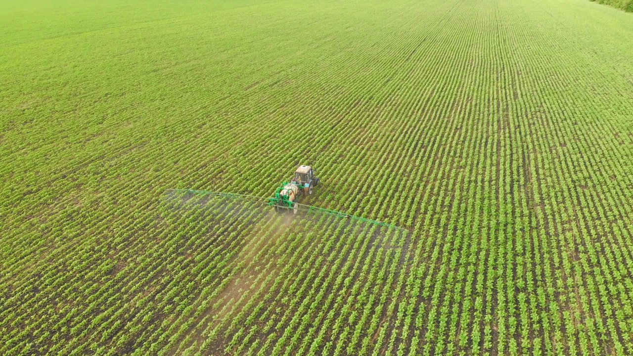 空中镜头。日落时分，农药喷雾器拖拉机在一大片绿色的田野上工作。航拍照片，旁边是一辆拖拉机在麦田里喷洒防病剂。农民喷洒大豆田。视频下载