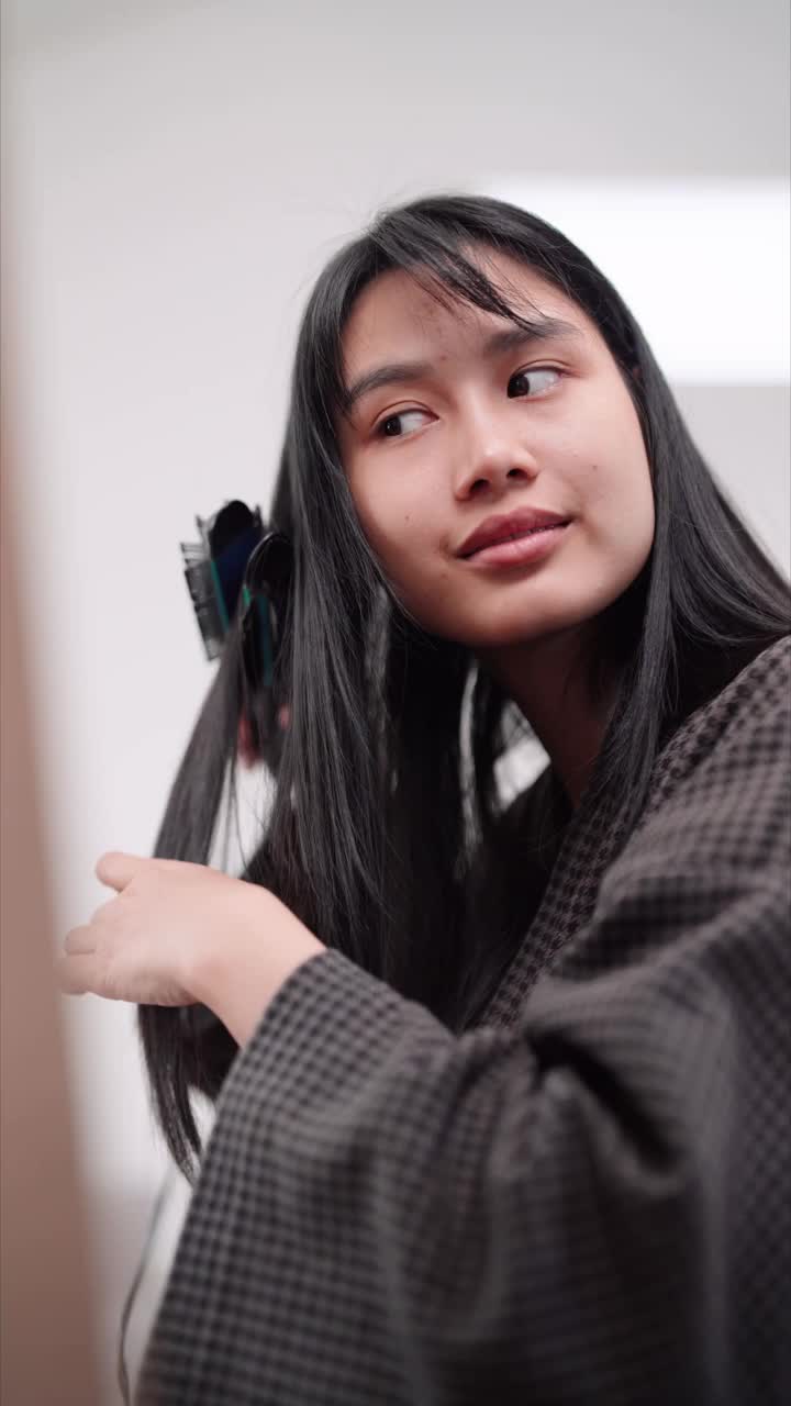 一名亚洲妇女在家里洗完头发定型后，在大镜子前使用直发器使头发变得光滑。展示自己的美容习惯，提高销量视频素材