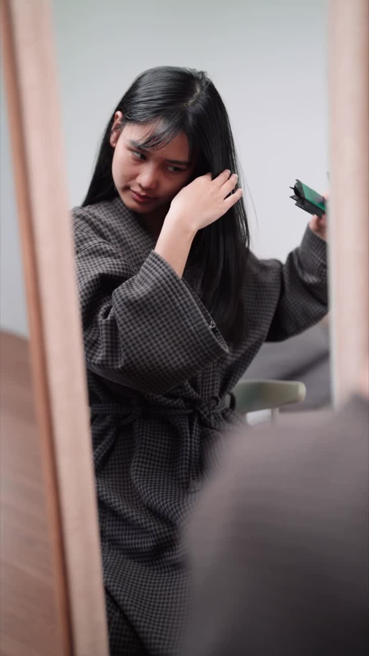 一名亚洲妇女在家里洗完头发定型后，在大镜子前使用直发器使头发变得光滑。展示自己的美容习惯，提高销量视频素材