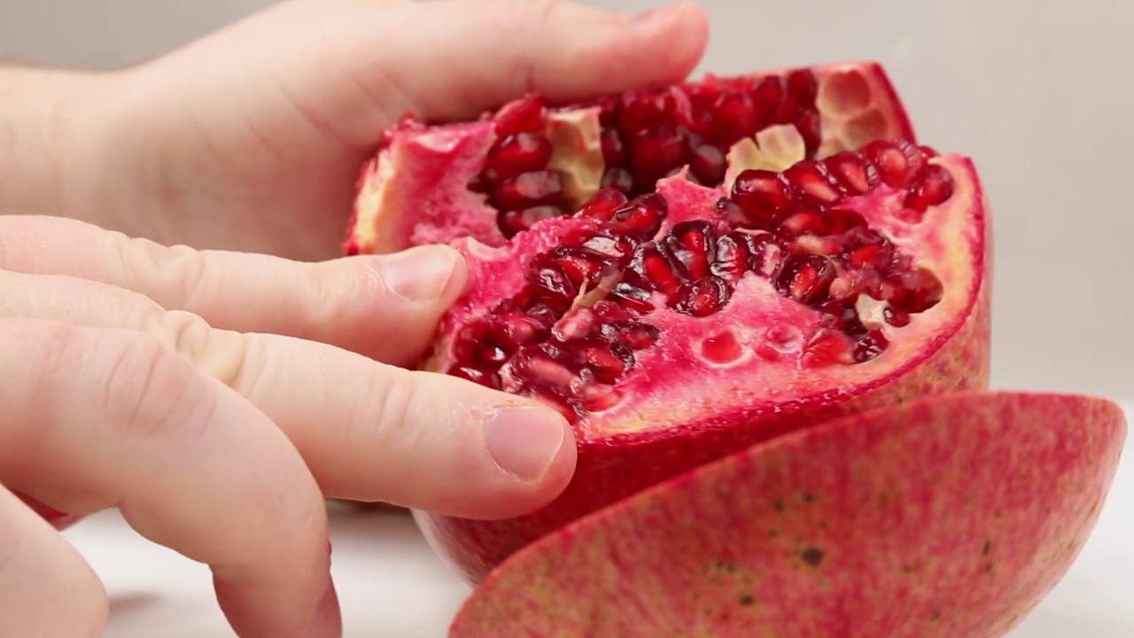 人的手把一个成熟的、多汁的、开胃的石榴果实掰成小块。视频下载
