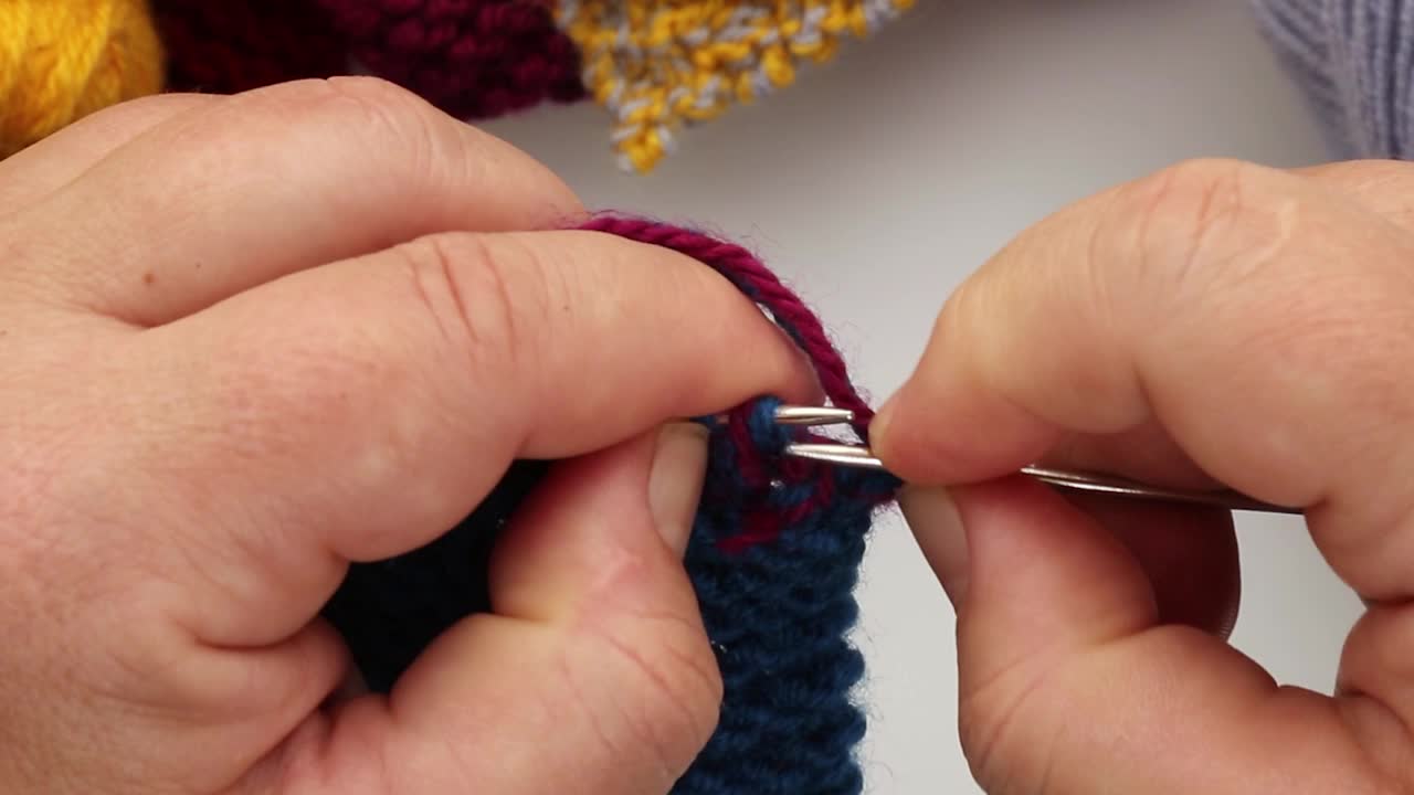 一位妇女正在用蓝色和红色的毛线编织一件毛织品视频下载