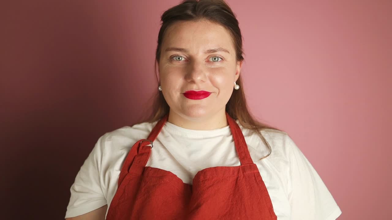 穿着红色围裙的女服务员手持椒盐卷饼街头小吃工作室拍摄的粉红色背景照片。高质量的全高清镜头视频下载