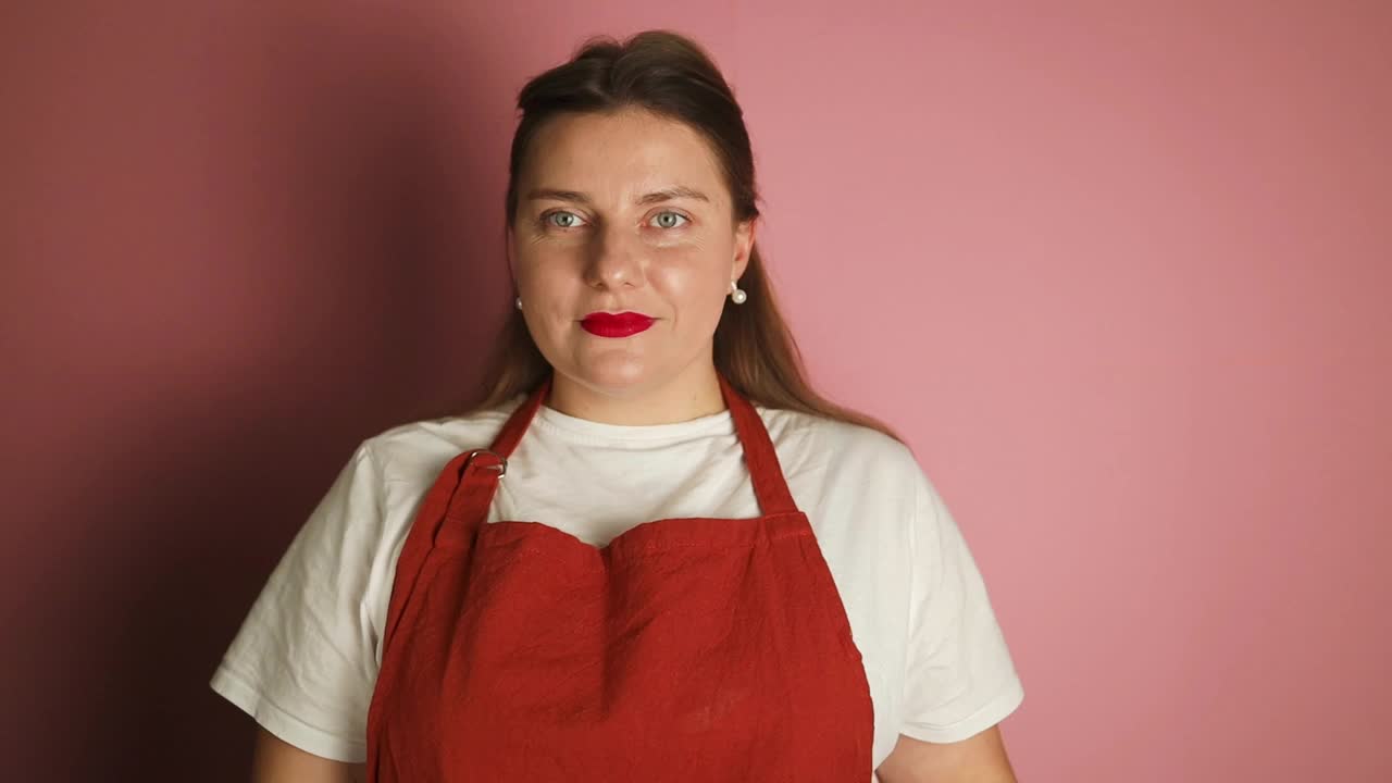 穿着红色围裙的女服务员手持椒盐卷饼街头小吃工作室拍摄的粉红色背景照片。高质量的全高清镜头视频下载