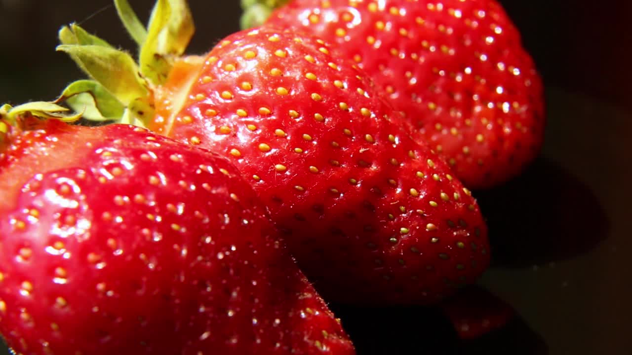 三个草莓在光滑的黑色表面上旋转。视频下载