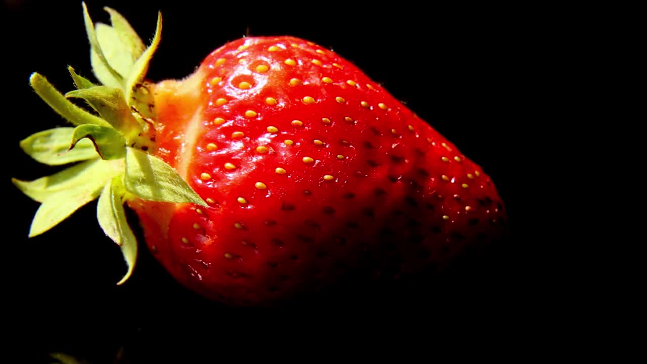 一个红色的草莓在光滑的黑色表面上躺着旋转。视频下载
