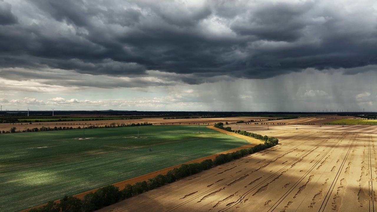 漆黑的天空和大片的雨云笼罩着田野。远处下着大雨。沿着耕地飞行。视频下载