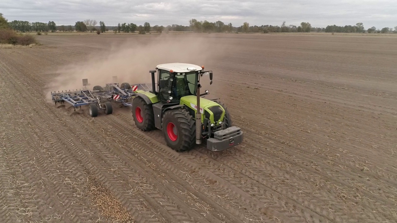 拖拉机耕作，翻耕着一片干燥的马铃薯田，夏季土壤干燥干旱，拖拉机带着一团尘土视频下载