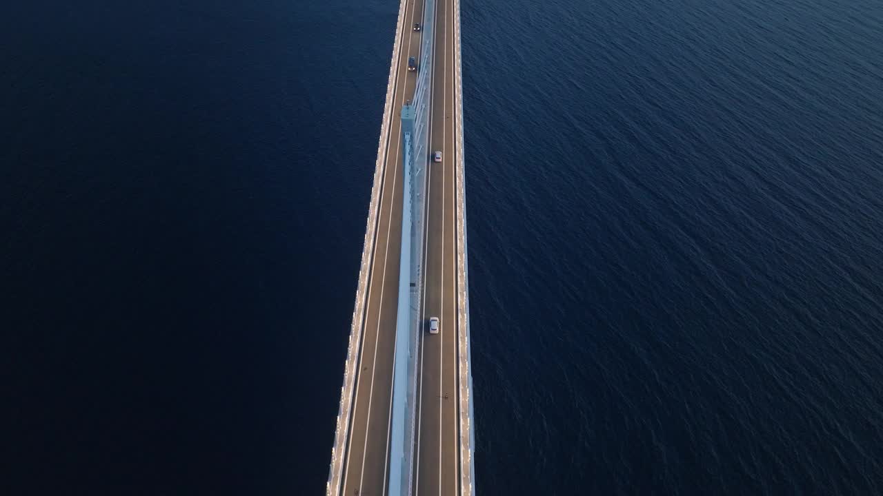 从上到下的鸟瞰图，俯瞰夜晚深蓝色的大海上的现代桥梁。汽车驶过地中海上的桥梁。视频素材