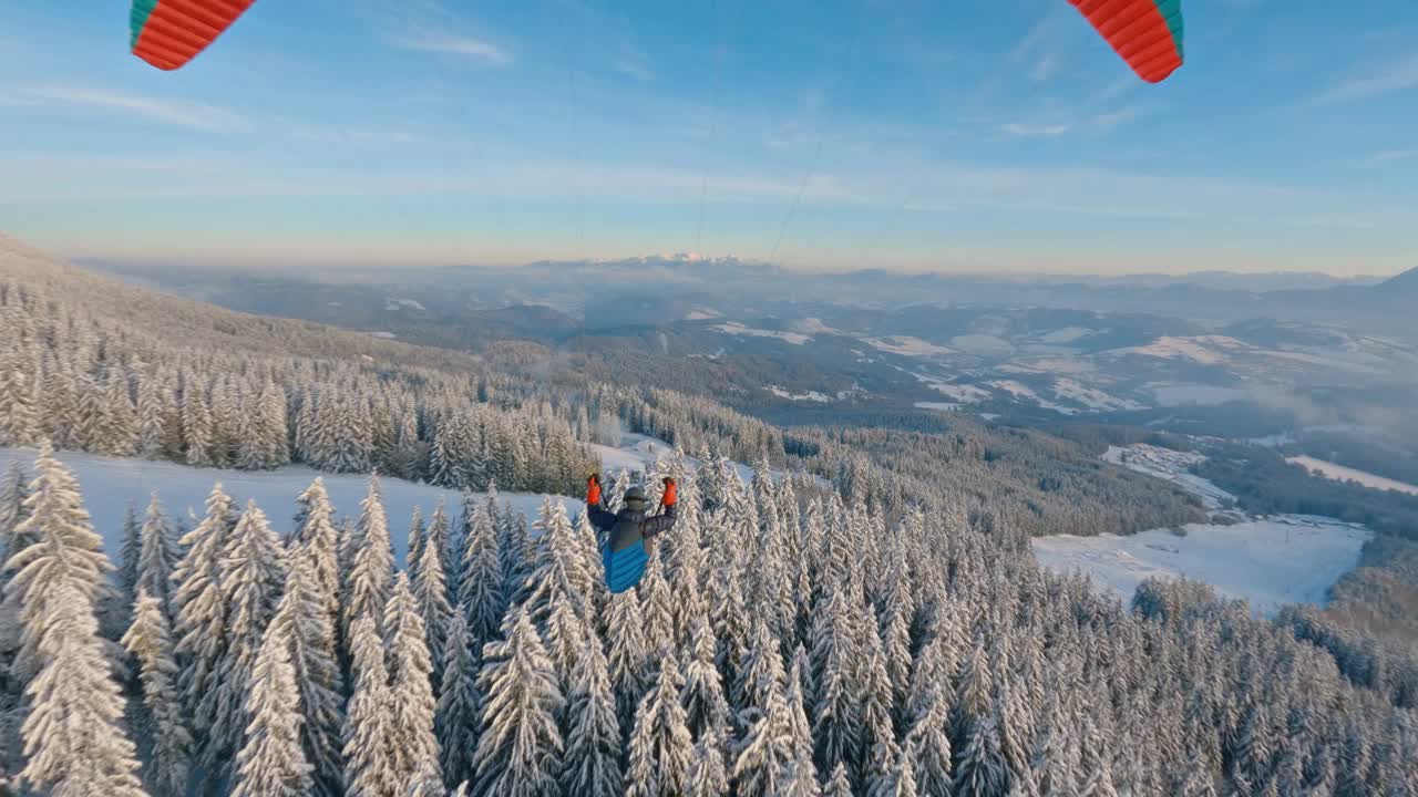 滑翔伞飞行在白雪皑皑的森林山脉，在冬天的日出仙境自然，自由飞行肾上腺素视频下载