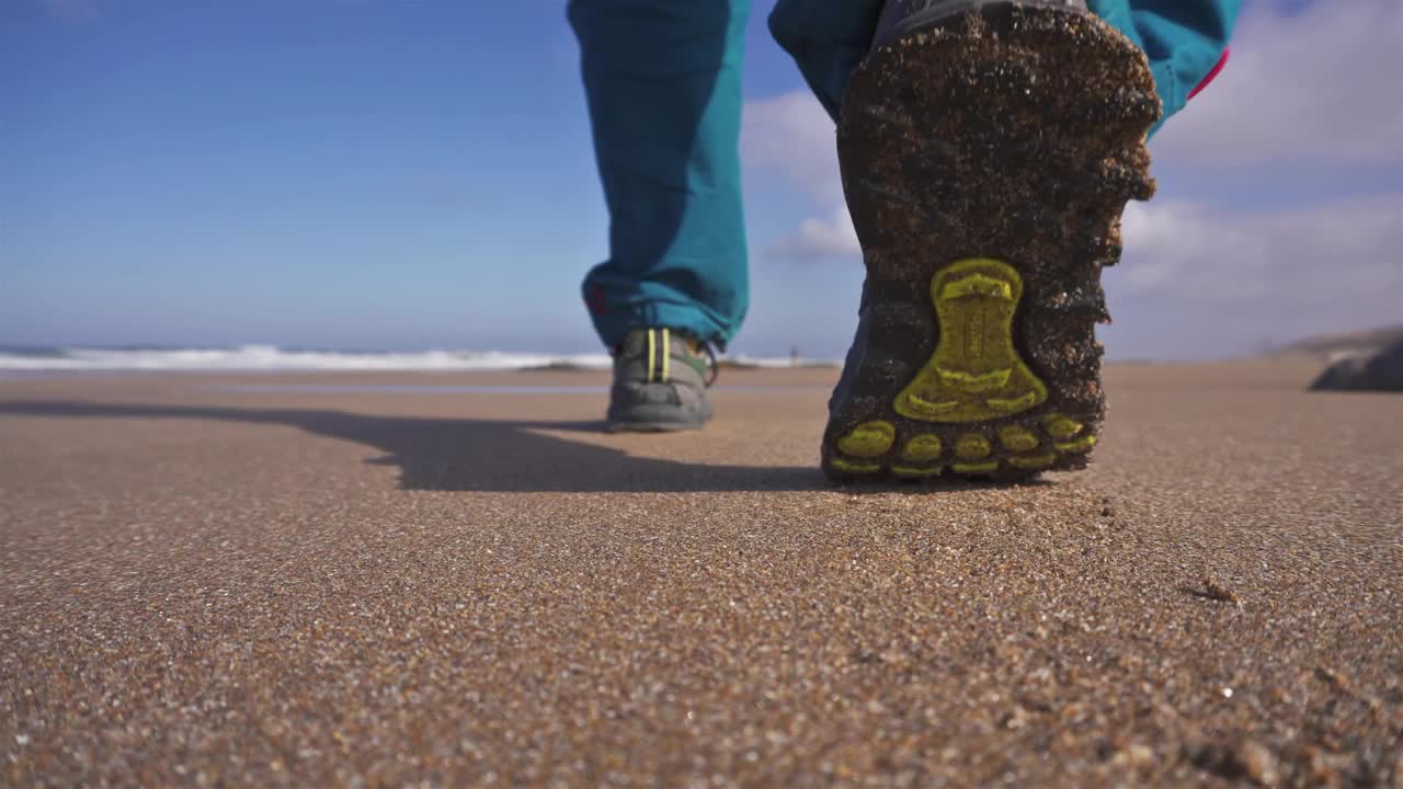 蓝色裤子和棕色夹克的男子走在沙滩上在阳光明媚的海洋海岸，低角度的看法，旅游假期的背景视频下载
