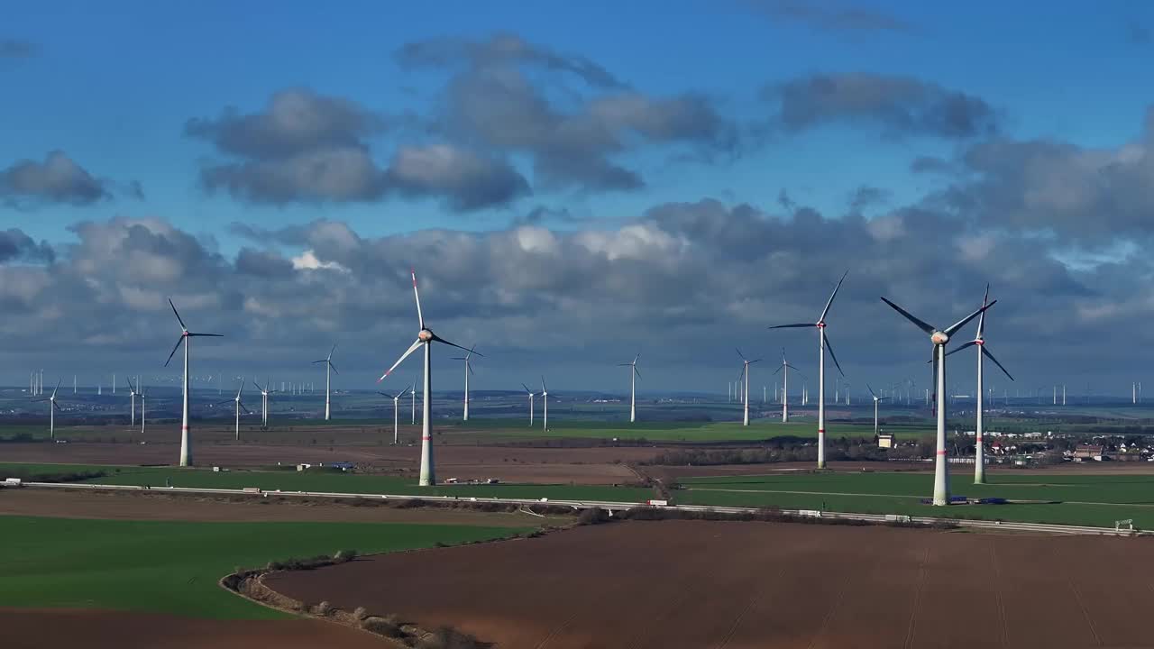 在乌云前的风力发电场的长焦镜头。
风力涡轮机在前景和地平线上。一条高速公路穿过这片风景。在田野上空缓慢飞行。视频下载