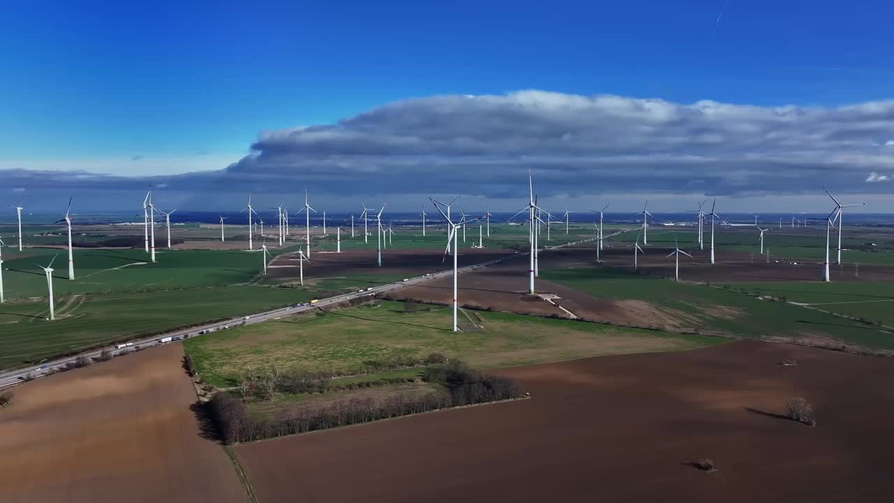 拥有不同类型风力涡轮机的大型风力发电场。一条高速公路穿过风电场。耕地和荒地。新建风力涡轮机。视频下载