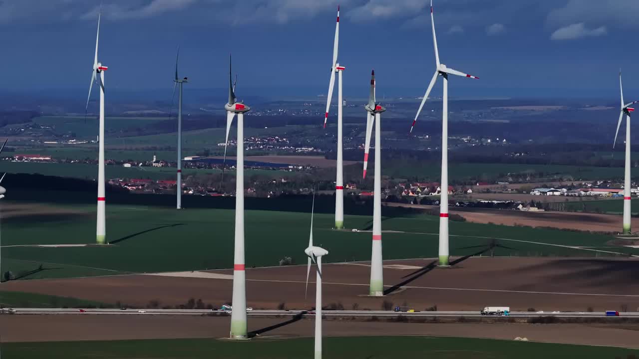 一个大型风电场的风力涡轮机的超远摄镜头。横向飞行经过不同类型的风力涡轮机。一条高速公路穿过风电场。视频素材