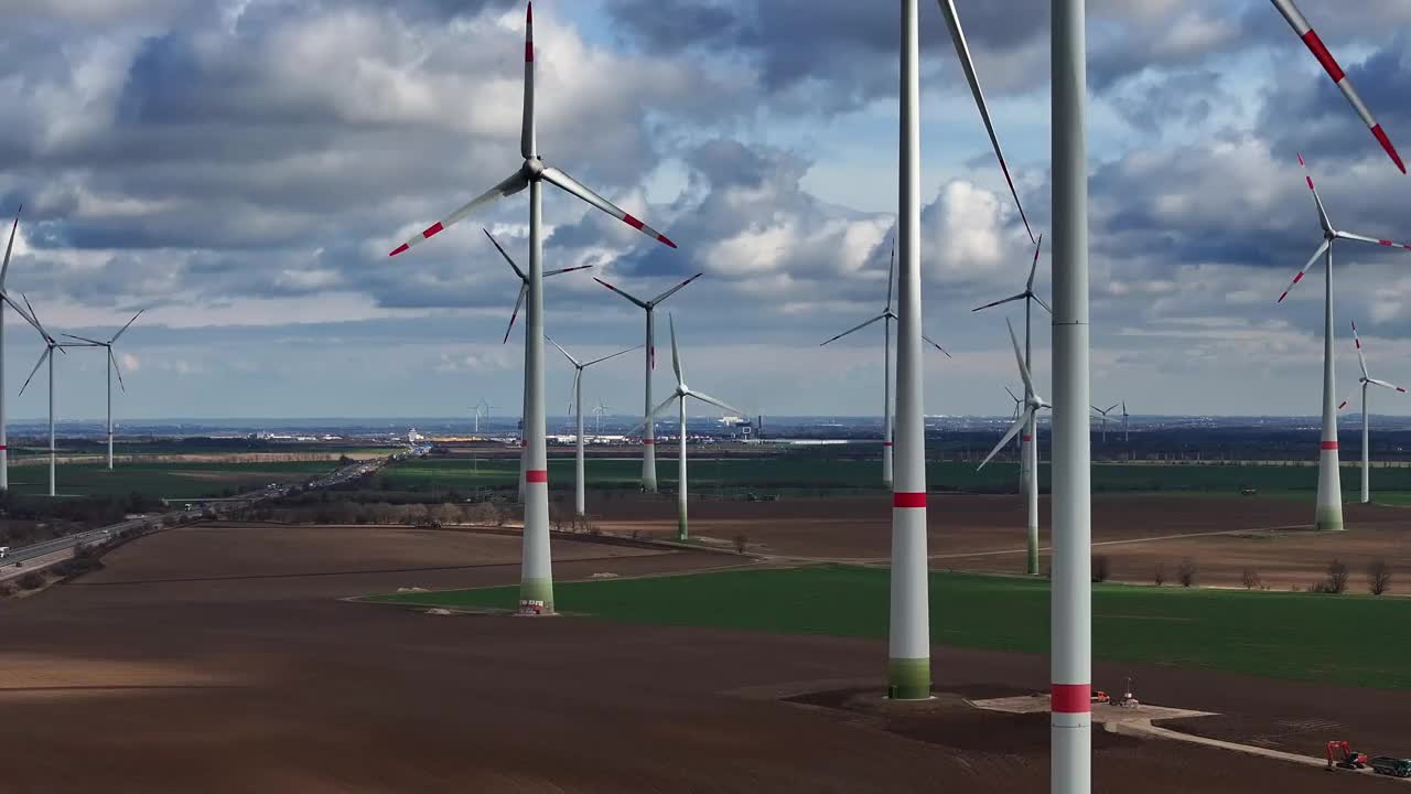 风力发电厂风力涡轮机的远摄照片。飞上贡多拉。几个风力涡轮机一个接一个地建造起来。在风力涡轮机旁边有一条高速公路。视频下载
