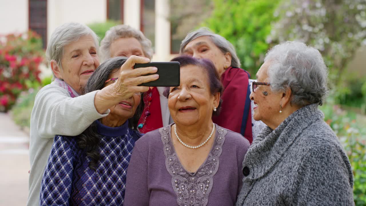 一群上了年纪的朋友站在养老院的花园里用手机自拍。快乐的老年女性在大自然中用智能手机一起视频通话。视频下载