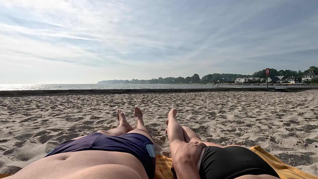海滩。这对夫妇正在晒日光浴。一个男人和一个女人的腿在大海的背景下。视频下载