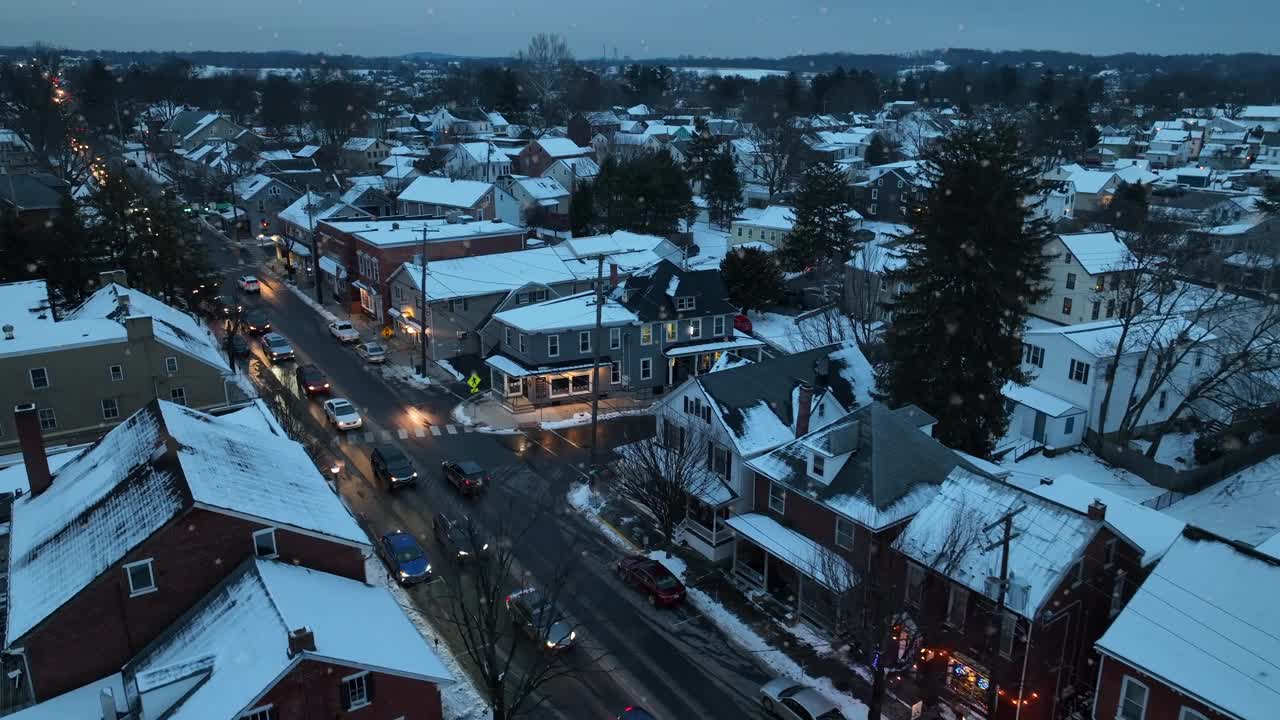 美国城市的冬天，雪花纷飞。傍晚住宅和公寓楼的航拍照片。黄昏时主干道上的交通。暖光店面窗户。远景。视频下载