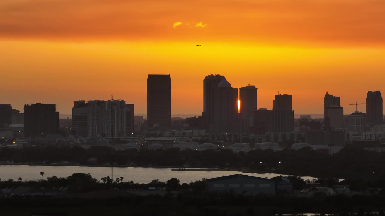 商用喷气式飞机在美国佛罗里达州坦帕市市中心日落景观上空起飞。现代美国大都市高耸的摩天大楼引人注目的天际线视频下载