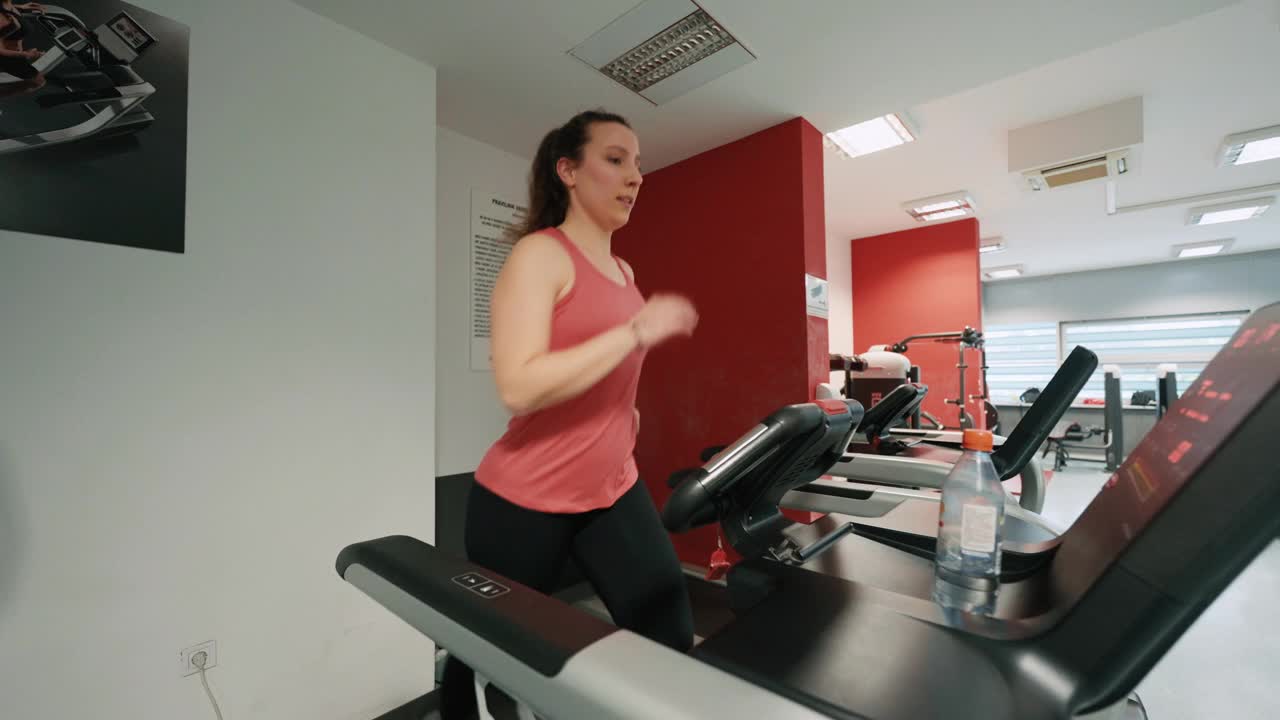 手持拍摄的坚定的年轻女子穿着运动服在跑步机上跑步在现代健身房视频下载