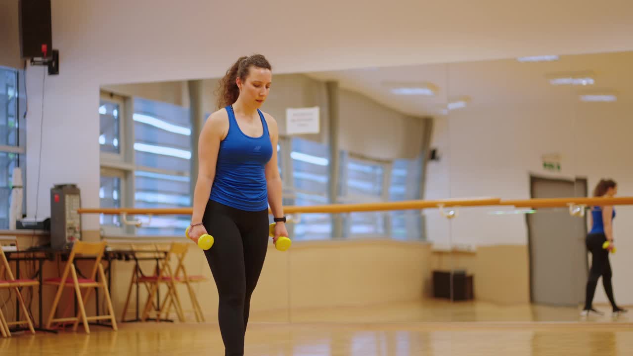 手持拍摄的年轻女子穿着运动服，在宽敞健身俱乐部的台阶平台上用哑铃锻炼视频下载