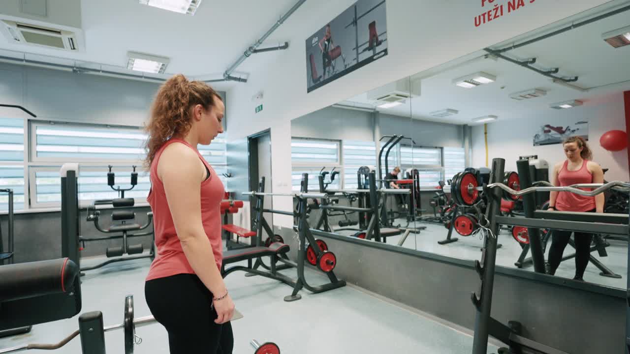 手持拍摄运动的年轻女子在运动服与杠铃在镜子前在现代健身房锻炼视频下载