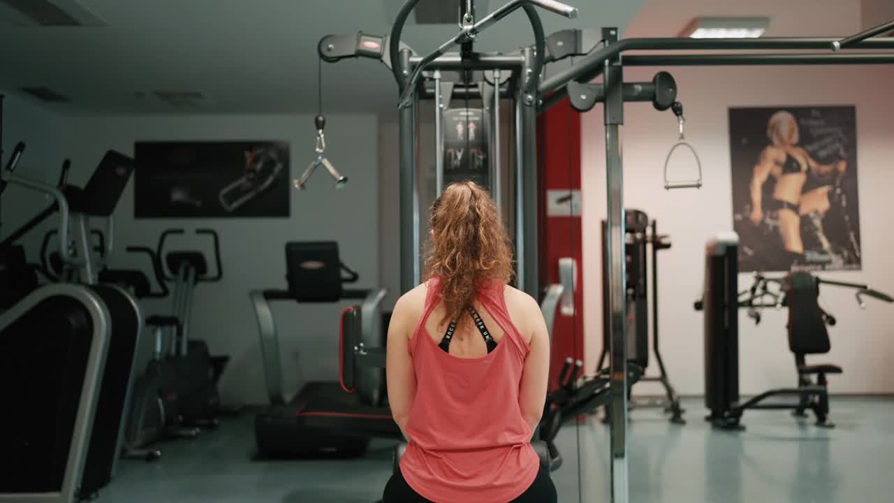 手持拍摄的运动女性在健身房使用拉下器械的后视图视频下载