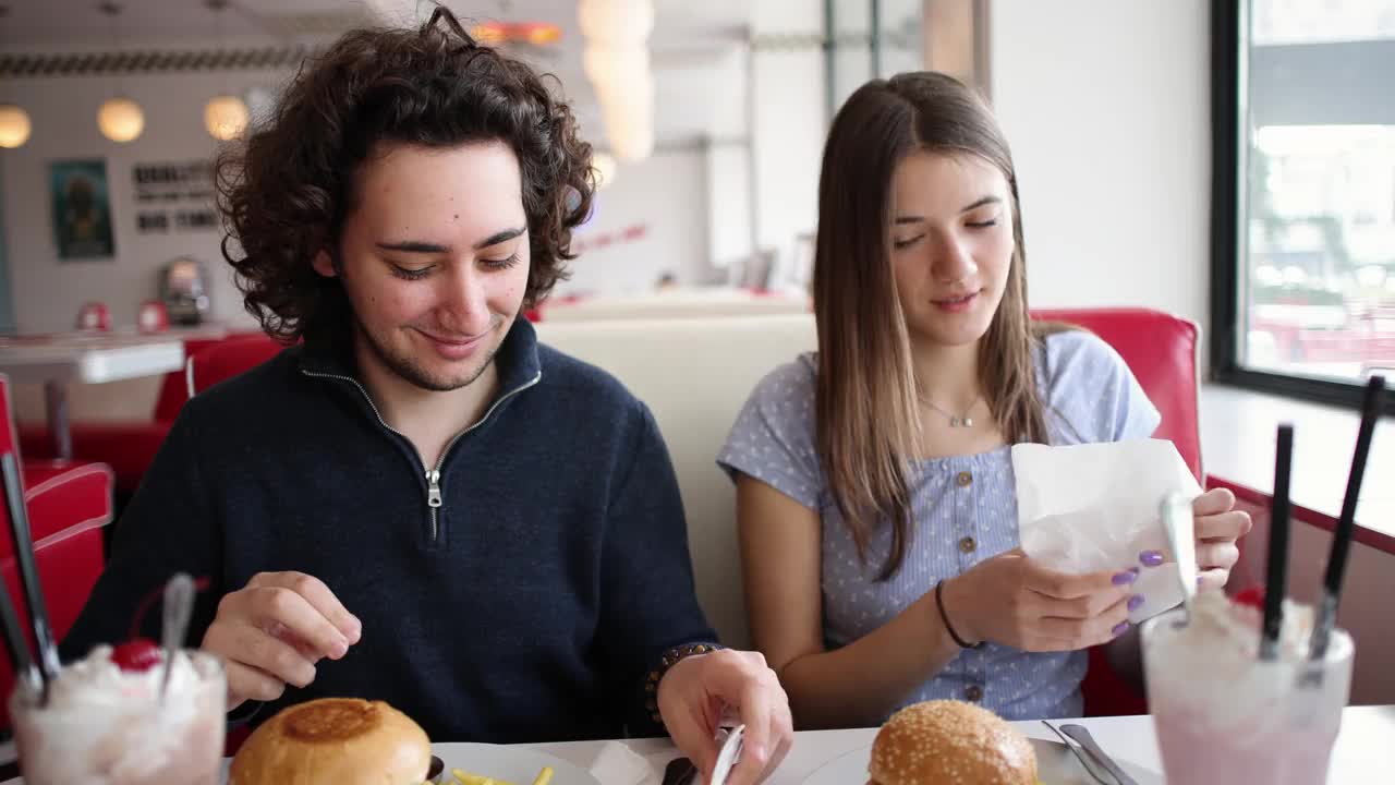 年轻的白人夫妇在复古的快餐店里吃汉堡和奶昔视频下载