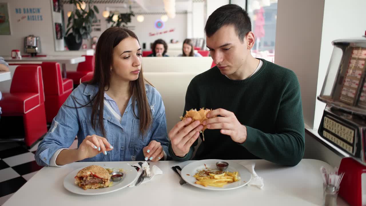 年轻夫妇在复古快餐店吃薯条和汉堡视频下载