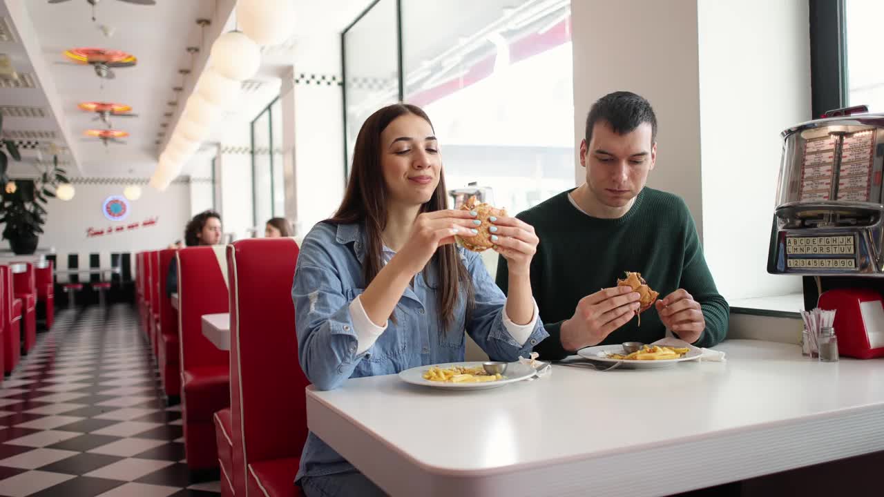 一对快乐的白人夫妇在复古的快餐店里吃薯条和汉堡视频下载