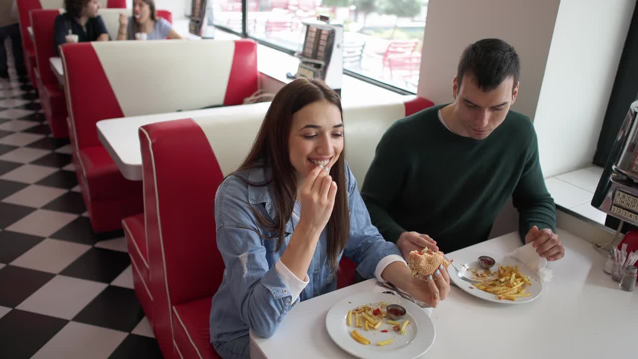 男女朋友在复古的快餐店吃薯条和汉堡视频下载
