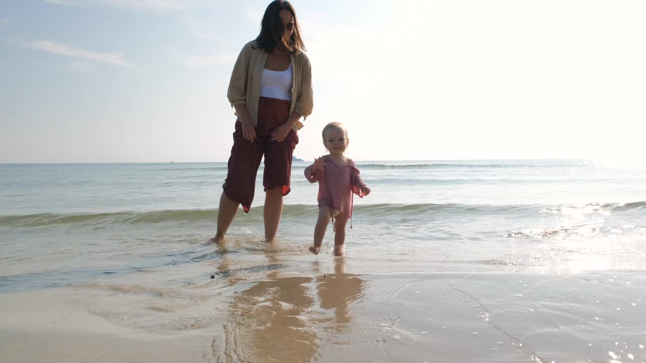 女婴和妈妈在沙滩上在海水中散步视频下载