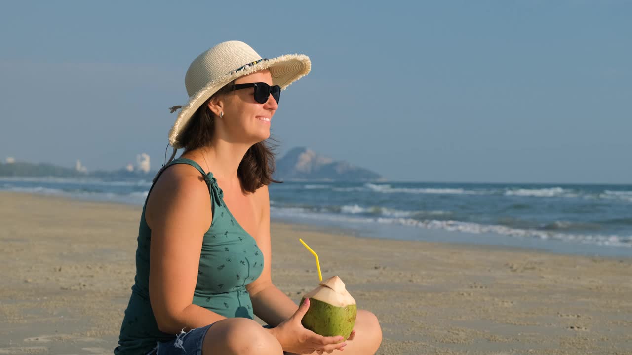 在沙滩上喝椰子汁的快乐女人视频下载