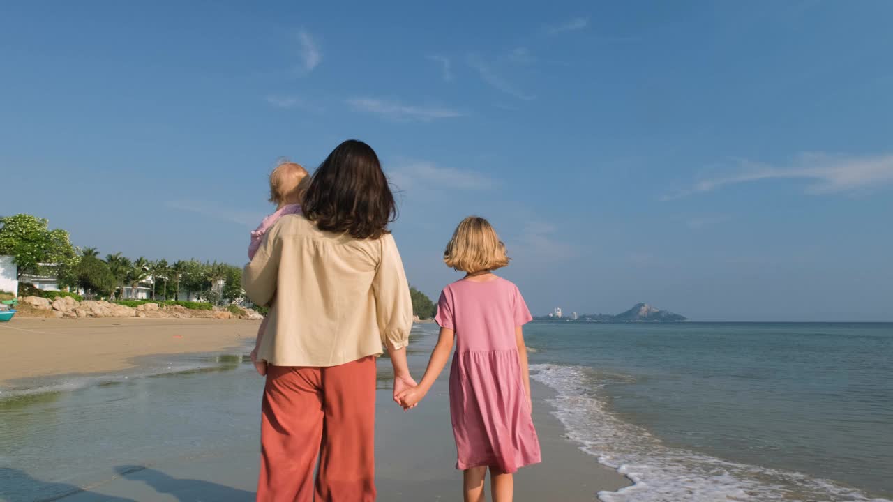 母亲和孩子沿着海岸散步的后视图视频下载