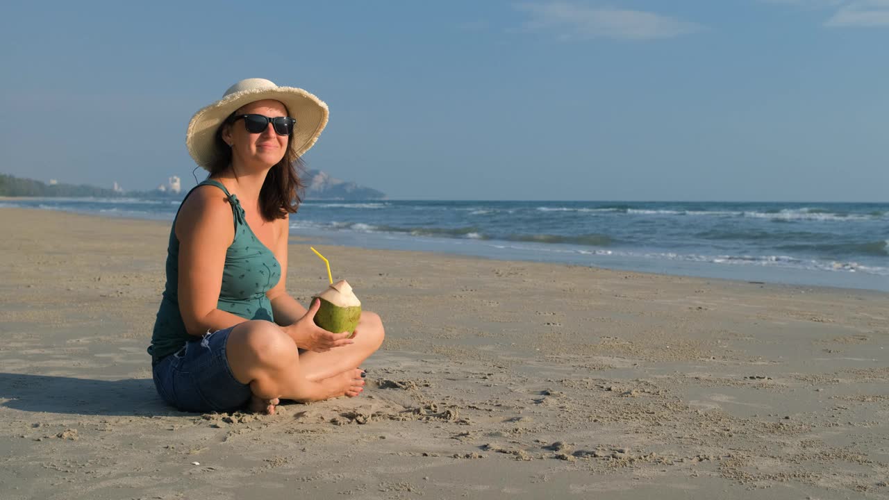 戴草帽的女人在沙滩上喝椰子汁视频下载