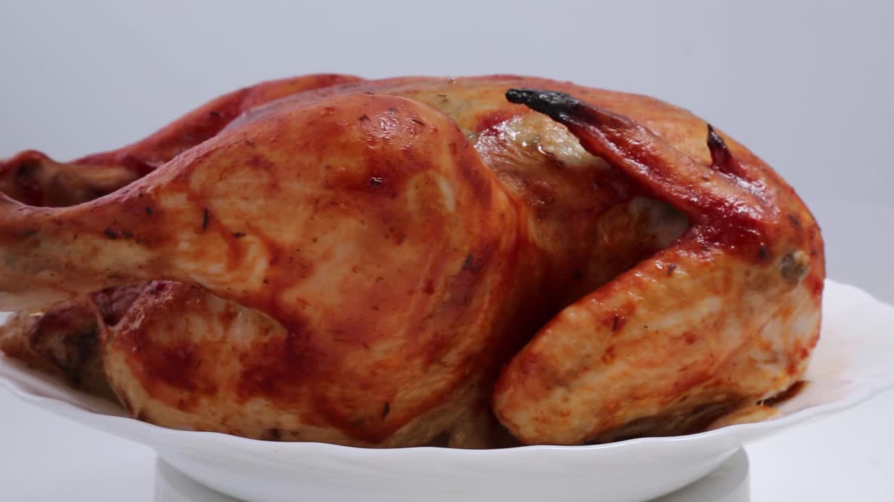 一整只外皮酥脆的烤鸡在白色盘子里旋转。视频下载
