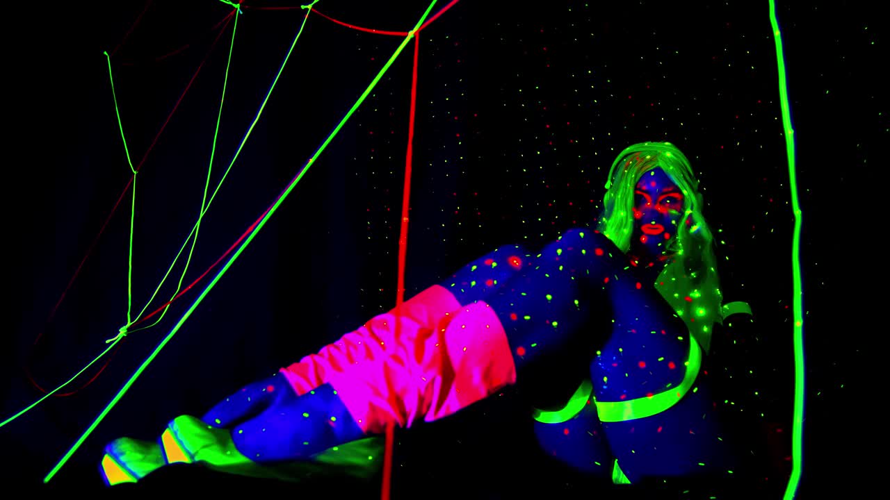 一个女人穿着发光的衣服摆姿势，在紫外线下发出明亮的光视频下载