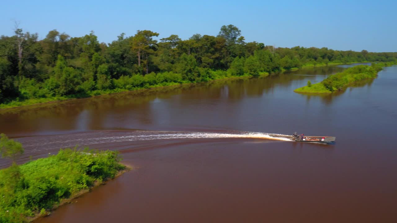 航拍拍摄的人在摩托艇上移动的波纹河在绿色景观- Bayou Vista，德克萨斯州视频下载