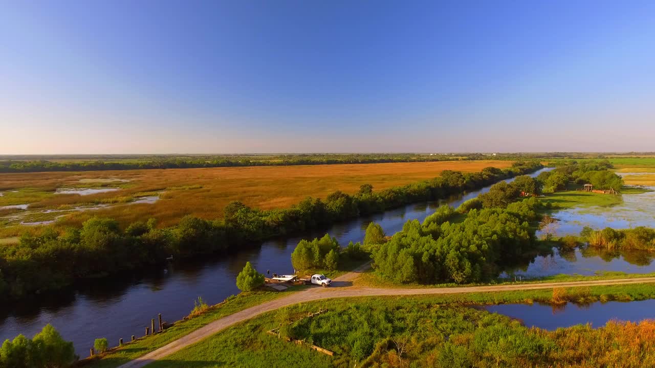 空中平移拍摄的皮卡车推动摩托艇在河，无人机飞越绿色景观在阳光明媚的一天- Bayou Vista，德克萨斯州视频下载