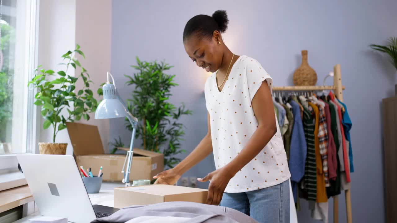 一位黑人女性小企业主正在打包衣服，她通过网站将其作为二手物品出售视频素材