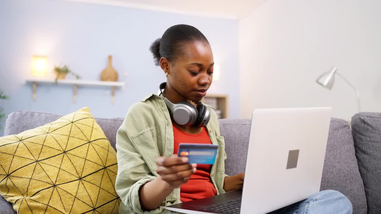 年轻的黑人女性用信用卡在笔记本电脑上网购视频下载