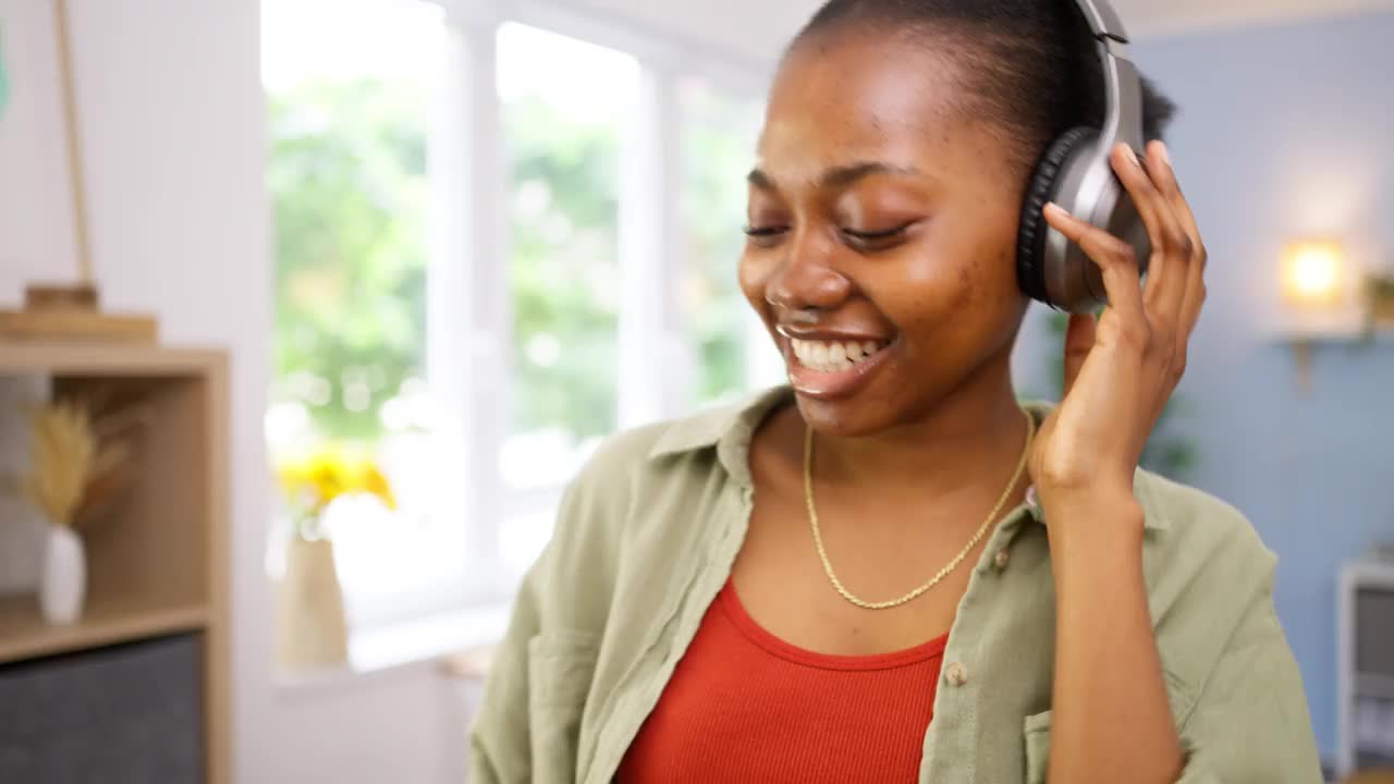 快乐的黑人年轻女子在客厅里一边听着无线耳机里的音乐一边跳舞视频素材