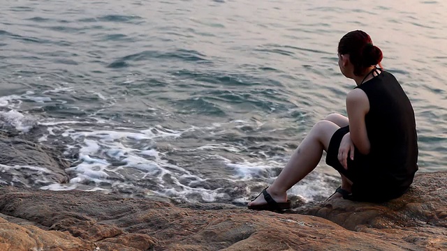 孤独的女人坐在一块岩石上，看着大海视频素材